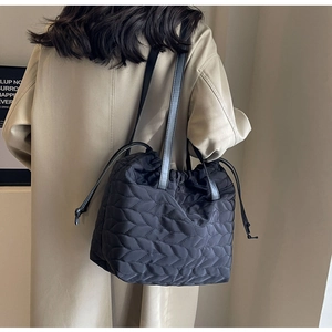 Detail view of a black quilted drawstring shoulder bag with leaf pattern stitching on fabric
