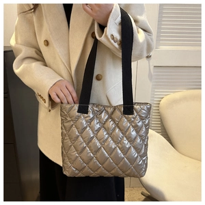 Detail of silver metallic quilted handbag with a black wide strap on a model's arm
