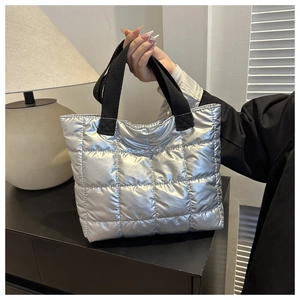 Detail of silver quilted tote bag with metallic finish and black woven strap handles