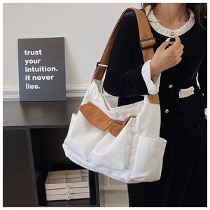 Detail of white canvas shoulder bag featuring brown flap pocket and decorative bow accent