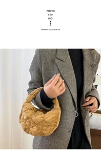 Close-up of ginger yellow quilted velvet hobo bag held by a model in a grey coat
