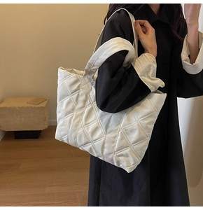 Macro view of the white quilted tote bag featuring a padded diamond pattern and long handles