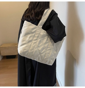 Close-up of white quilted tote bag featuring a padded texture and wide shoulder strap