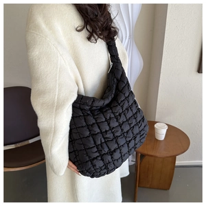 Gros plan du sac à bandoulière matelassé noir porté par un mannequin dans un décor sobre