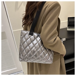Detail view of quilted silver tote bag with black strap on model in neutral setting