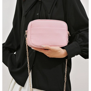 Chic pink pebble leather crossbody camera bag with gold chain strap shown on model
