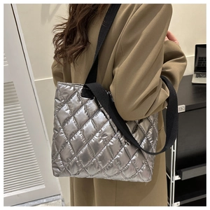 Detail of silver quilted tote bag with metallic finish and wide black fabric shoulder strap