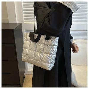 Close-up of a silver puffer tote bag with quilted texture and black fabric straps