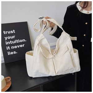 Detailed view of white canvas shoulder bag featuring multiple pockets and wide adjustable straps