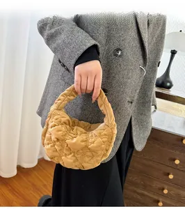 Close-up of a camel quilted plush crescent bag held by a model in a gray suit