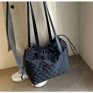 Detail of black quilted nylon tote bag with drawstring accents in a lifestyle setting