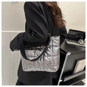 Detail of metallic silver quilted tote bag with black strap worn by a model in office