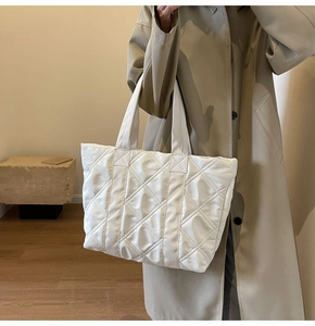 Detailed shot of white quilted tote bag worn by model in stylish trench coat