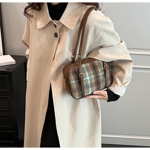 Close-up of retro plaid shoulder bag with brown leather trim and adjustable metal buckles