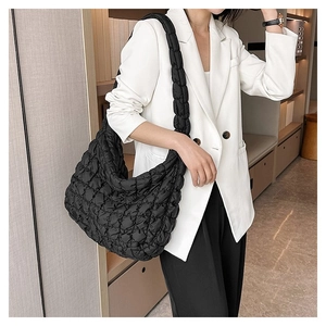 Close-up of black quilted cloud bag with pleated texture worn on shoulder with white blazer