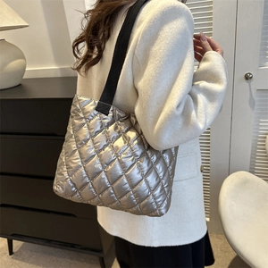 Silver quilted metallic tote bag with wide strap worn by model in a minimalist setting