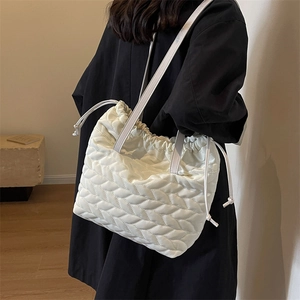 White quilted puffer tote bag with drawstring closure and slim straps on black coat