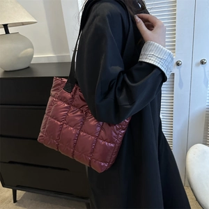 Chic burgundy quilted puffer tote bag with black straps worn by model in minimalist setting