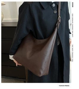 Detail of minimalist dark brown hobo bag worn with a black oversized coat in a home setting