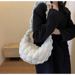 Detail of white quilted cloud crescent bag texture and wide strap on black coat