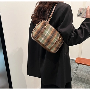 Close-up of a vintage plaid shoulder bag with brown leather trim on female model