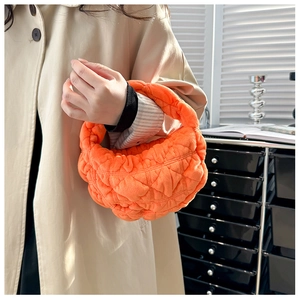Detail shot of bright orange quilted dumpling handbag featuring soft wavy texture