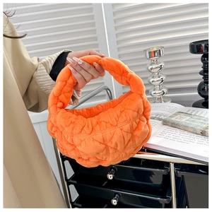 Detail of a bright orange quilted velvet handbag featuring soft plush texture and mini handle