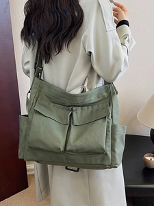 Olive green canvas messenger bag with large front pockets and adjustable strap on a model