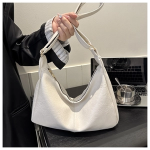 Close-up of a white crescent shoulder bag with natural leather texture and gold hardware