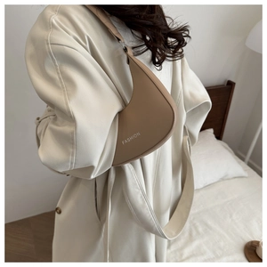 Detail of minimalist beige croissant shoulder bag with printed FASHION text in warm indoor setting