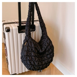 Quilted black dumpling bag hanging on a suitcase handle, showing light texture and space