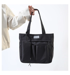 Detail of black nylon tote bag with functional pockets and Fashion label on white background