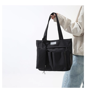 Close-up of black nylon tote bag featuring front utility pockets and side zipper pouch