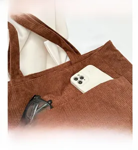 Close-up of brown corduroy tote bag featuring a front pocket for phone and glasses