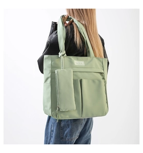 Detail of light green nylon tote bag featuring front pockets and fashion tag detail
