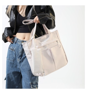 Detail of high-capacity cream nylon tote bag with multiple pockets and mini pouch charm