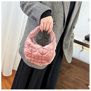 Pink quilted cloud bag in velvet texture held by a model in a grey herringbone suit