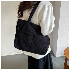 Close-up of black corduroy shoulder tote bag with front utility pockets and ribbed texture