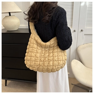 Détail du sac fourre-tout matelassé beige porté à l'épaule sur un tricot texturé chic