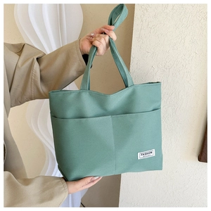 Dettaglio della borsa tote in tela verde salvia con doppie tasche frontali ed etichetta in tessuto