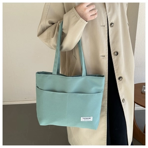 Dettaglio della borsa tote in tela verde menta con tasche frontali ed etichetta logo