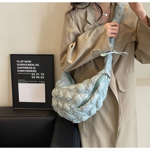 Close-up of a light blue quilted crescent bag with wide shoulder strap on a model