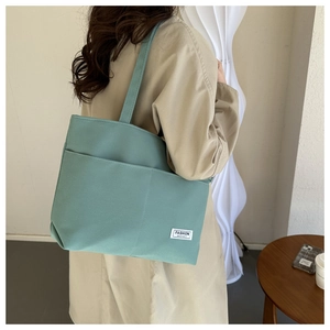 Dettaglio della borsa tote in tela verde acqua con tasca frontale indossata dal modello