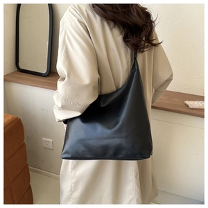 Close-up of a large black glossy PU leather tote bag worn with a beige trench coat