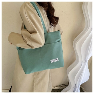 Dettaglio della borsa tote in tela verde scuro con tasca frontale e trama dell'etichetta