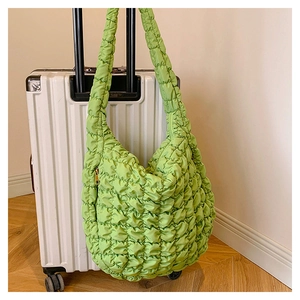 Detail of green quilted puffer hobo bag with gold zipper hanging on luggage