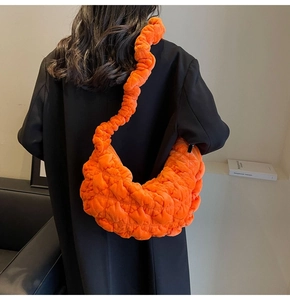 Detail of bright orange quilted crescent bag with designer ruched shoulder strap