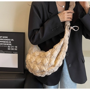 Minimalist beige quilted crescent bag worn crossbody with adjustable drawstring strap