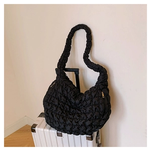 Detail of black cloud pleated crossbody bag resting on a white metal suitcase