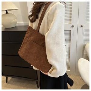 Brown corduroy shoulder tote bag with front pockets worn by a model in a cozy interior